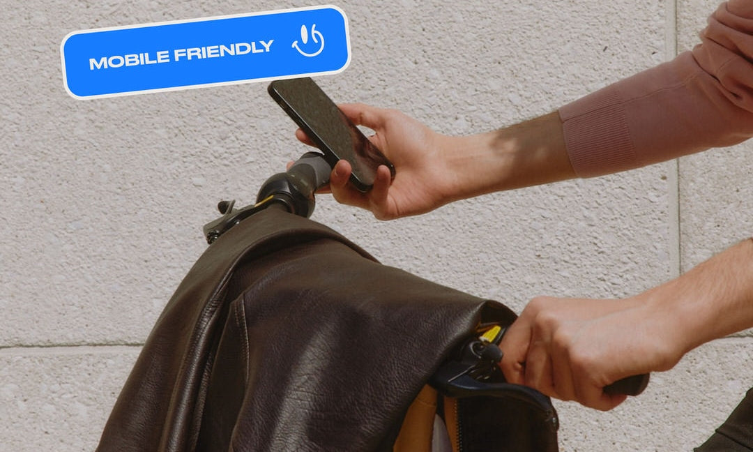 A photograph of a person pushing a cart, with a leather jacket hanging over it, holding a cell phone, along with a graphic badge on top with the words "mobile friendly" and a happy face.