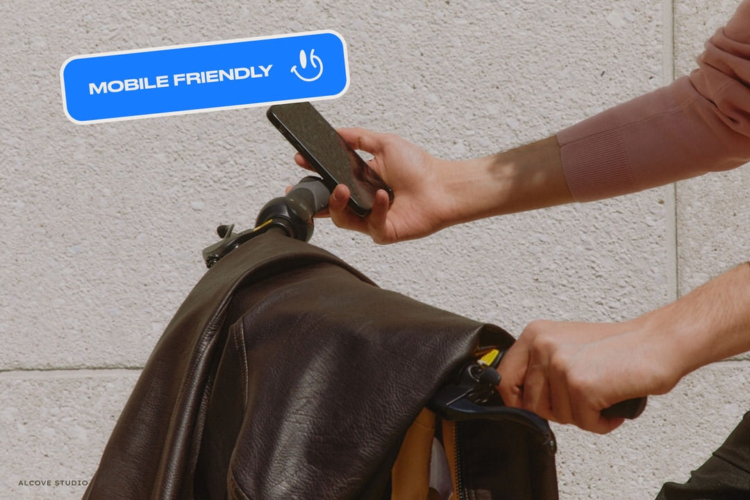 A photograph of a person pushing a cart, with a leather jacket hanging over it, holding a cell phone, along with a graphic badge on top with the words "mobile friendly" and a happy face.